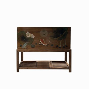 May include: A wooden chest with a painted design of lotus flowers and a fish. The chest is on a stand with a shelf.