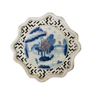 May include: A white ceramic plate with a blue and white landscape design. The plate has a scalloped edge and a cut-out design around the outer edge.