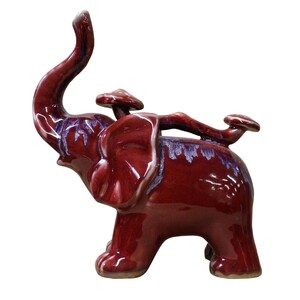 May include: A burgundy ceramic elephant figurine with a raised trunk and three mushroom-shaped decorations on its back.