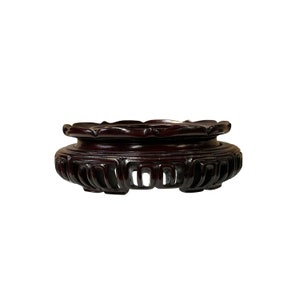 May include: A dark brown wooden plant stand with intricate carvings. The stand has a circular top and a rounded base.