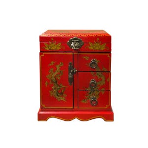 Puede incluir: Un joyero de madera roja con detalles dorados y un diseño de fénix decorativo. La caja tiene una puerta de armario, dos cajones y un compartimento superior. La ferretería es de latón antiguo. Solución de almacenamiento decorativa.