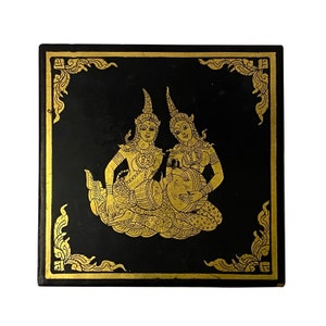 May include: Square black decorative box with a gold ornate border and a gold illustration of two figures playing instruments. The figures are dressed in traditional attire. The box has a glossy finish.