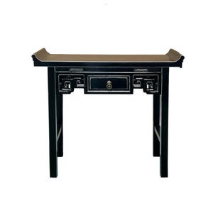 May include: A black wooden console table with a single drawer and decorative cutouts. The table has a rectangular top with curved edges and four straight legs. The drawer features a round, ornate handle.