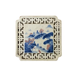 May include: A white ceramic tile with a blue and red landscape scene framed by a white lattice border.