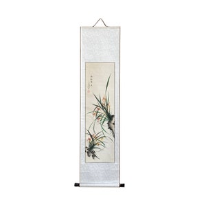 Puede incluir: Una pintura tradicional china en rollo que representa una delicada disposición de orquídeas blancas con hojas verdes. La pintura está hecha con tinta negra y acuarela sobre papel de arroz y está montada en un rollo de seda. El rollo está colgado en una pared con una varilla de madera en la parte superior e inferior.