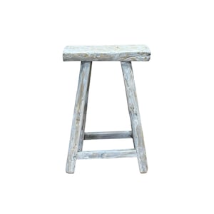 May include: A whitewashed wooden stool with a simple, rustic design. The stool has a rectangular seat and a triangular base.