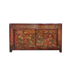 May include: A rectangular wooden cabinet with a dark red finish, featuring two doors decorated with hand-painted floral motifs in orange, green, and yellow. The frame is adorned with a gold-colored geometric border pattern and two small metal ring pulls.