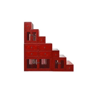May include: A red wooden cabinet unit with a stepped design. The unit features multiple drawers and cabinet doors with vertical slat detailing. The cabinet is painted in a solid red color and has a vintage aesthetic.