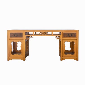 May include: A wooden desk with a traditional Chinese design. The desk has two drawers and two open shelves on each side. The desk is made of light brown wood and has a dark brown finish.