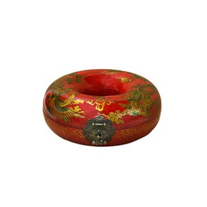 May include: A red, donut-shaped decorative box with gold dragon and phoenix designs. The box has a metal clasp and is likely of Asian origin. The box is a vibrant red color.