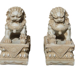 May include: A pair of white stone foo dog statues with intricate details. Each statue is sitting on a square base with a decorative design.