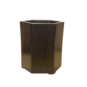 Peut inclure: Un pot de fleurs hexagonal en bois brun foncé. Le pot a une finition lisse et polie.