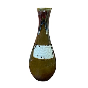 May include: A brown ceramic vase with a white design on the front. The vase has a narrow neck and a wide base.