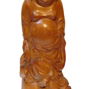 Peut inclure: Statue en bois de Bouddha souriant. La figure est représentée debout, avec un grand ventre et des robes fluides. La statue est sculptée dans un bois brun clair et repose sur un socle décoratif.