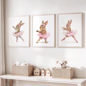 Puede incluir: Tres impresiones enmarcadas de acuarelas de conejitos bailarines de ballet con tutús rosas y zapatillas de ballet. Las impresiones se exhiben sobre una mesa blanca con cestas de mimbre, casas de juguete y peluches.