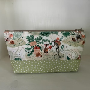 Peut inclure: Une trousse zippée en tissu crème imprimé de souris et de grenouilles jardinant parmi des radis et des champignons. La partie inférieure est en tissu vert clair à pois blancs. Une petite breloque perlée est suspendue à la fermeture éclair.
