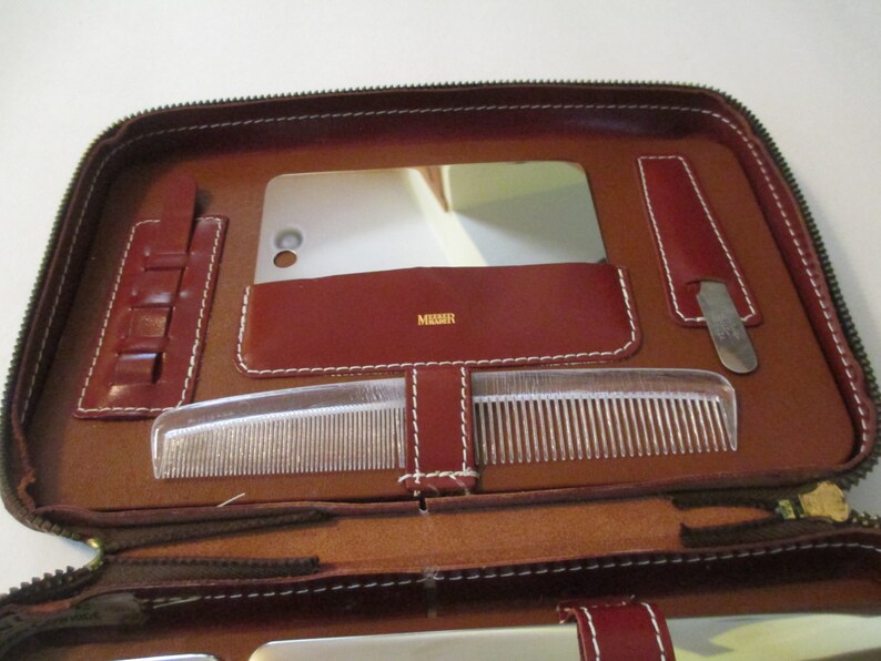 May include: Brown leather travel kit with a zipper closure. The kit is open and contains a mirror, a comb, a nail file, and a small container with multiple compartments.
