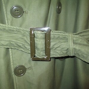 May include: A green military-style jacket with a belt and metal buckle. The jacket has two large buttons on the front.