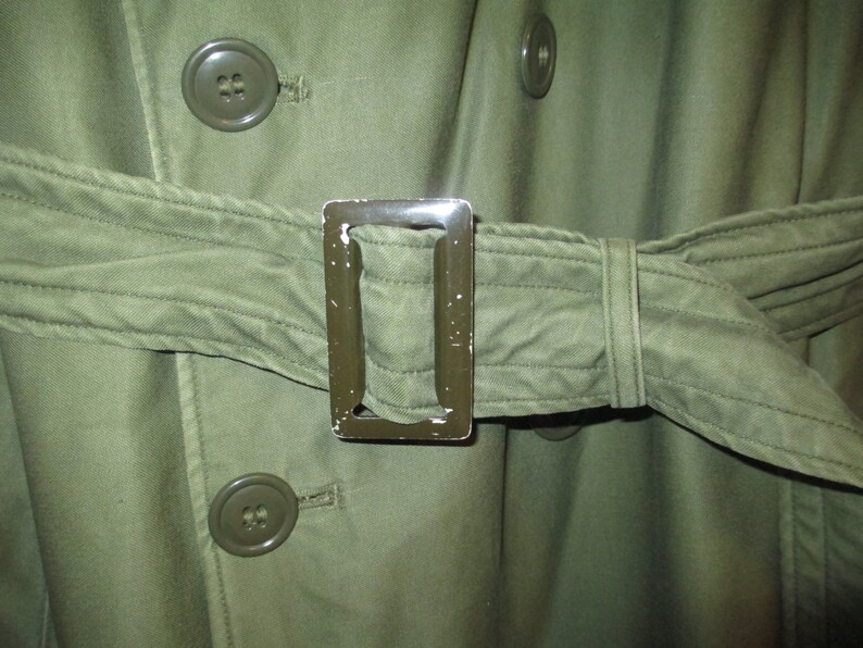 May include: A green military-style jacket with a belt and metal buckle. The jacket has two large buttons on the front.