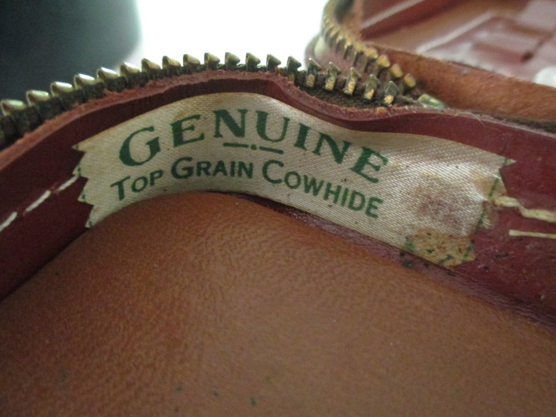 May include: Close-up of a brown leather zippered pouch with a white label that reads "GENUINE TOP GRAIN COWHIDE" in green lettering.