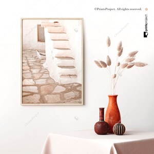 K&ouml;nnte beinhalten: Ein gerahmtes Foto eines wei&szlig;en Geb&auml;udes mit einem Steinweg, der zu einer Treppe f&uuml;hrt. Das Foto ist in einem hellen Holzrahmen und h&auml;ngt an einer wei&szlig;en Wand.