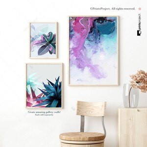 May include: Three framed prints, two with abstract watercolor designs in shades of pink, blue, and white, and one with a close-up of tropical plants with green and blue leaves. The prints are hanging on a white wall above a wooden chair and stool.