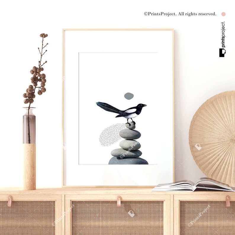 May include: A black and white magpie perched on a stack of grey stones. The stones are arranged in a pyramid shape. The background is white.