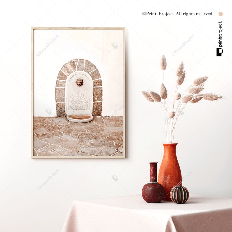 K&ouml;nnte beinhalten: Ein gerahmter Druck einer Steinbrunnen mit einem Bogen und einem Fliesenboden. Der Brunnen ist in einer neutralen Farbpalette aus Beige und Braun gehalten. Der Druck h&auml;ngt an einer wei&szlig;en Wand.