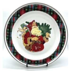 May include: A white ceramic plate with a red and green plaid border. The center of the plate features a vintage illustration of Santa Claus carrying a Christmas tree and gifts.