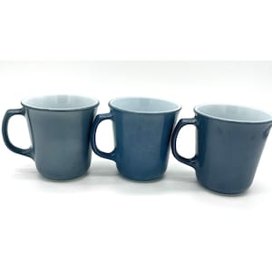 Puede incluir: Tres tazas de cerámica azules con interiores blancos. Las tazas tienen una forma redondeada y un asa en el lateral.