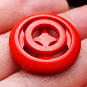 May include: A red plastic button with a four-pointed star design in the center.