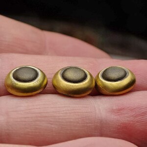 May include: Three gold-colored buttons with a dark brown center. The buttons have a textured surface.