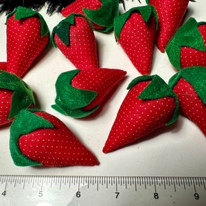 May include: A group of ten red and green felt strawberries. The strawberries are all about 3 inches long and have a white polka dot pattern.