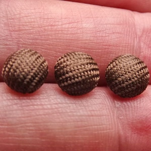 May include: Three brown fabric buttons with a woven texture.