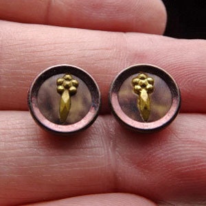 May include: Pair of round, brown and gold buttons with a raised design. The buttons have a textured surface and a gold rim.