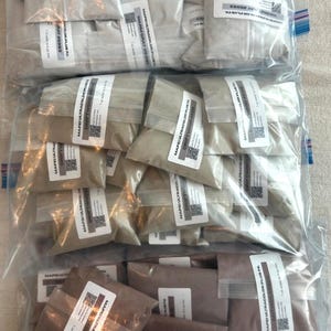 May include: Multiple small, clear plastic bags filled with Mapei Ultracolor Plus FA grout powder in three distinct colors: warm gray, driftwood, and a darker brown shade. Each bag features a white label with product text and a QR code.