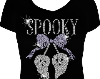 May include: Black V-neck t-shirt with a rhinestone design. The design features the word "SPOOKY" above a bow and two ghost figures. The ghosts and bow are embellished with rhinestones, creating a sparkling effect. A Halloween-themed apparel item.