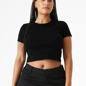 May include: A solid black short-sleeved crop top with a crew neckline. The garment features a fitted silhouette that ends above the waistline, constructed from a plain fabric. The design is simple, featuring no patterns, graphics, or additional embellishments.