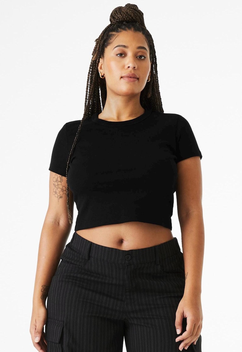 May include: A solid black short-sleeved crop top with a crew neckline. The garment features a fitted silhouette that ends above the waistline, constructed from a plain fabric. The design is simple, featuring no patterns, graphics, or additional embellishments.