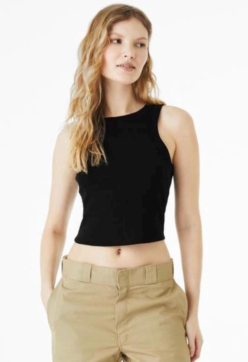 May include: A black sleeveless tank top with a high neckline and a cropped hemline, paired with khaki-colored trousers featuring a wide waistband and a visible front button closure. The top is made of a solid black fabric with a ribbed texture.