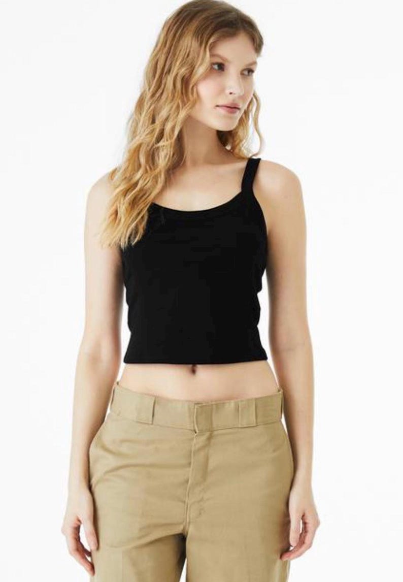 May include: A black sleeveless crop top with a scoop neckline and wide shoulder straps, paired with khaki-colored trousers featuring a structured waistband, a front zipper closure, and visible belt loops, creating a simple and functional outfit.