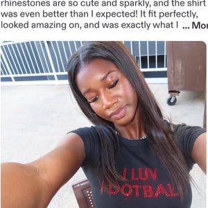 May include: A black short-sleeved t-shirt featuring the red rhinestone text I LUV FOOTBALL on the chest. The shirt has a crew neckline and a fitted silhouette. The red rhinestones are arranged to form the letters of the text clearly.