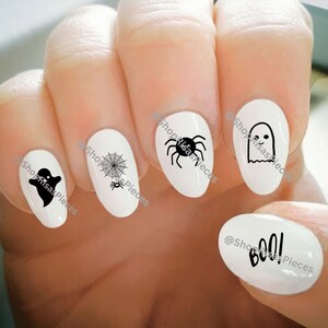 May include: White nail art featuring black Halloween-themed designs. The designs include a ghost, spider, spiderweb, and the word "boo!". The nails are oval-shaped and have a glossy finish.