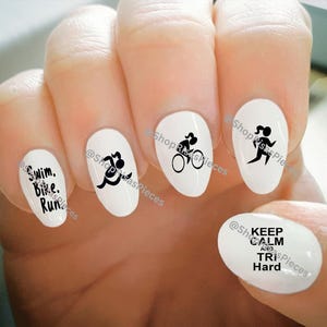 Op de afbeelding: Set van vijf witte ovale nagelstickers met zwarte tekst en afbeeldingen. De stickers bevatten de tekst "Swim. Bike. Run." en afbeeldingen van een zwemmer, een fietser, een hardloper en de tekst "Keep Calm and Tri Hard."