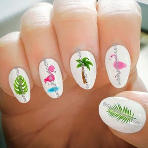 May include: Five oval-shaped nail decals with tropical designs. The decals feature a pink flamingo, a palm tree, and two green tropical leaves. The decals are on a white background and have the text "@ShopRisaPieces" on each decal.