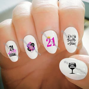 May include: White nail art stickers with various designs for a 21st birthday. Designs include the number 21 in pink, a crown, balloons, and phrases like "I'm 21, Buy Me a Drink!" and "Drink Bitches".