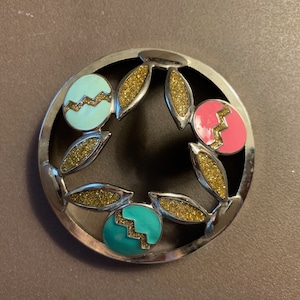 May include: A silver candle jar lid with a black background and three colorful Easter eggs with gold glitter accents.