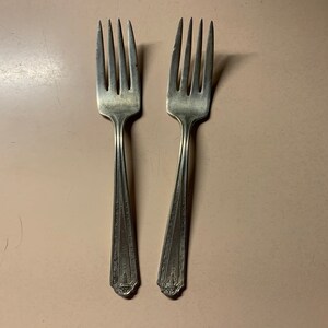 May include: Two silver forks with ornate designs on the handles.