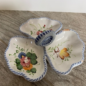 May include: A white ceramic serving dish with three sections and a central handle. Each section is decorated with colorful floral designs and a blue and white striped border. The handle is blue and white.