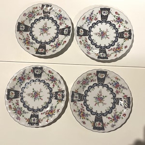 May include: Set of four white porcelain plates with a blue and gold floral design. The plates have a scalloped edge and a central design with a floral motif.